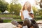 Photo of happy sunlit woman screaming and rejoicing while sitting on bench in green park on summer day, and holding smartphone