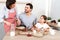 Photo of hard working wife, husband and their daughter sit together at kitchen table, going to eat delicious pancakes