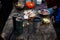 Photo of hiker`s breakfast wooden table with bread, bacon , cans, other meals and hot mugs at the forest camp. People