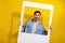 Photo of impressed cheerful man dressed jeans shirt tacking portrait paper photo frame isolated yellow color background