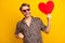 Photo of impressed sweet guy wear leopard outfit arm dark eyewear rising fists holding red heart isolated yellow color