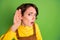 Photo of interested curious young girl hold palm ear listen wear yellow shirt overall isolated green color background