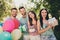 Photo of joyful brown haired happy friends at birthday party wear cones hold gift box cake balloons outside in picnic