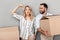 Photo of joyful european couple in casual clothing holding flat keys and carrying cardboard boxes
