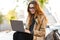 Photo of joyous woman working on laptop while sitting on bench in city street