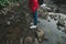 Photo of the legs of a girl in a red raincoat standing on a stone in the middle of a mountain river. Evening photo of a female