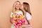 Photo of lovely mother and daughter wear pink green t-shirt hold tulips kiss cheek 8-march isolated on beige color