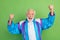 Photo of lucky funky senior man wear sportive suit rising fists smiling isolated green color background