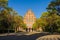 Photo of main building of University from entrance gate on blue autumn sky and yellow and green foliage on trees. Architecture of