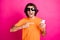 Photo of man hand direct forefinger hold telephone wear orange t-shirt sunglass isolated pink color background