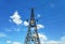 Photo of a metal power transmission tower with wires on a background of bright blue sky with white clouds