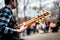 Photo of musician playng on six string fretless bass guitar on the street in front of people.
