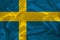 Photo of the national flag of the state of Sweden on a luxurious texture of satin, silk with waves, folds and highlights, close-up