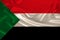 Photo of the national flag of Sudan on a luxurious texture of satin, silk with waves, folds and highlights, close-up, copy space,