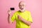 Photo of old positive cheerful excited grandfather wear lime t-shirt point finger at credit card isolated on pink color