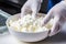 Photo of a person mixing cottage cheese in a bowl wearing white gloves. Preparation of cottage cheese for cheese production.