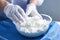 Photo of a person mixing cottage cheese in a bowl with white gloves. Preparation of cottage cheese for cheese production. Handmade