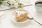 Photo of piece of cake on saucer dessert spoon spectacles white cup of coffee and flowers on white keyboard on white desk