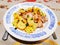 Photo porcelain plate with a blue pattern and lying on it potatoes with chicken and herbs with a knife and fork on the tablecloth