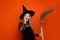Photo portrait of attractive blonde teen woman hold broom excited dressed black halloween clothes isolated on orange