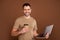 Photo portrait brunet man in pastel t-shirt working with computer drinking coffee isolated brown color background