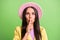 Photo portrait of brunette girl in pink hat keeping finger near lips silent secret isolated on vibrant green color