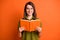 Photo portrait of cheerful female student wearing glasses keeping book smiling isolated on vibrant orange color