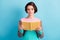 Photo portrait of clever girl holding yellow book in two hands isolated on pastel light blue colored background