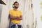 Photo portrait of curious guy with folded hands smiling on street listening music in headphones wearing yellow t-shirt