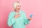 Photo portrait of happy laughing grandmother reading information on cellphone hand on chest isolated on pastel pink