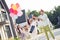 Photo portrait of married couple with children wearing party headwear. Father swings little boy by hands outdoors in