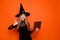 Photo portrait of pretty blonde teenager girl netbook showing thumb up dressed black halloween outfit isolated on orange