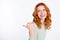 Photo portrait of red haired woman smiling curious showing thumb empty space recommending isolated white color
