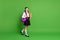 Photo portrait of schoolgirl going forward holding books in hand wearing violet backpack on shoulder isolated on vivid
