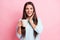 Photo portrait of smiling pretty woman surprised cheerful keeping mug with drink hand near face isolated on pastel pink