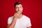 Photo portrait of surprised guy keeping secret closed mouth with hand staring blank space isolated bright red color