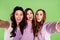 Photo portrait of three girlfriends showing tongue careless childish taking selfie blinking isolated on vivid green