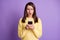 Photo portrait of upset nervous girl holding phone in two hands with open mouth isolated on vivid violet colored