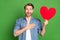 Photo portrait of young guy amazed in casual outfit keeping red heart shaped postcard hand on chest isolated on vibrant