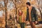 Photo of positive couple girl guy go in fall october foliage park hold hands wear season jackets rucksack