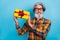 Photo of positive pretty retired man wear plaid shirt spectacles showing present box isolated blue color background