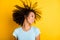 Photo of pretty adorable dark skin wavy lady wear blue t-shirt smiling wind blow hair isolated yellow color background