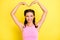 Photo of pretty adorable young woman pigtails wear tank top showing arms big heart isolated yellow color background