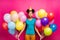 Photo of pretty funny dark skin lady hold many colorful air balloons blow noisemaker birthday surprise wear paper cone