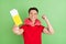 Photo of pretty lucky young man wear red t-shirt neck pillow holding tickets rising fist isolated green color background