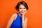 Photo of pretty shiny girl dressed blue top smiling arm cheek empty space isolated orange color background