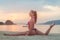 Photo in profile of slim fitness model with brown hair wearing bikini doing leg split exercise on beach at sunrise
