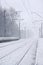 Photo of the railway station in the suburbs or the countryside. The railroad runs between dense rows of trees. Snow-covered platf