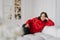 Photo of relaxed young woman dressed in warm knitted clothes, lies on comfortable sofa, enjoys domestic atmosphere, decorated New