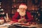 Photo of santa claus sit workspace take delivery service order phone wear hat sweater in north pole office indoors